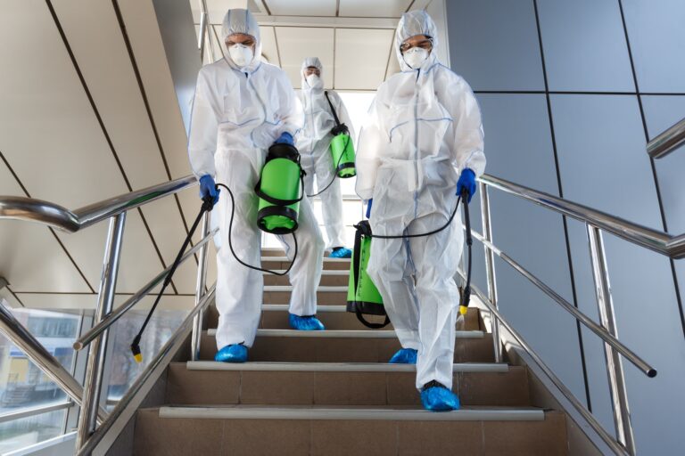 People wearing protective suits disinfecting stairs with spray